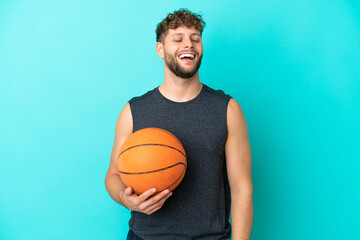 Handsome young man playing basketball isolated on blue background laughing