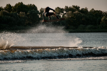 wonderful view of dynamic guy holding rope and jumping high with wakeboard over water