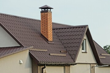 one large red brick chimney on a brown tiled roof of a private gray house with a window against the...