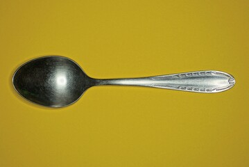 one old gray metal spoon lies on a yellow table