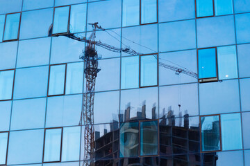 Blurred reflection of a construction tower crane in the glass windows of the building as in a...
