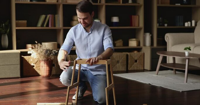 Do it yourself. Inspired millennial male homeowner renovate living room interior screw wooden shelf together. Skilled young man assemble flat pack furniture use simple tool hex key to fix details easy