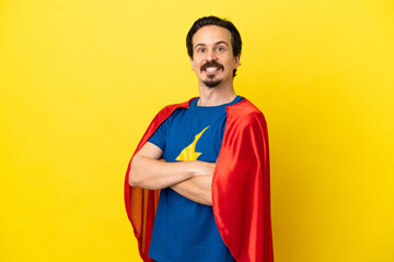 Young caucasian man isolated on yellow background in superhero costume with arms crossed