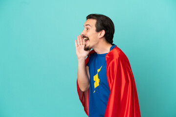 Super Hero caucasian man isolated on blue background shouting with mouth wide open to the side