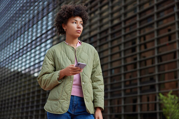 Photo of good looking woman wears jacket jeans holds mobile phone installs app updates profile in...