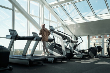 Back view of young active female running on treadmill in front of large window in contemporary leisure center
