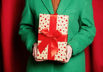 Woman in green jacket with holiday gift box on red curtains background