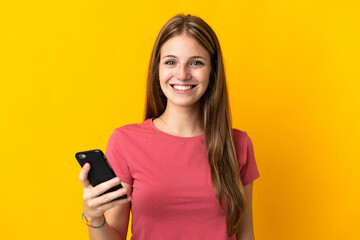 Young woman using mobile phone isolated on yellow background smiling a lot