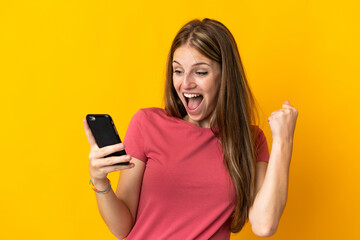 Young woman using mobile phone isolated on yellow background celebrating a victory