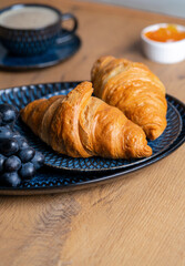 crispy croissant on a plate on a wooden table next to jam and orange juice, delicious breakfast. High quality photo