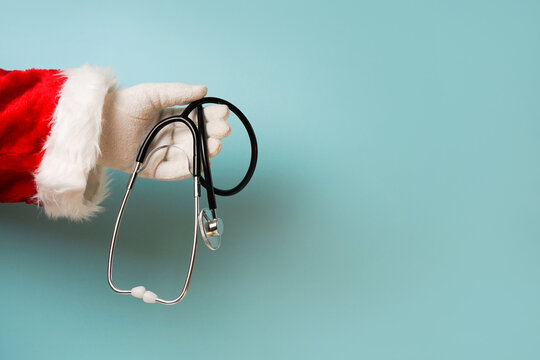 hand of santa claus holding stethoscope medical equipment on blue background, copy space