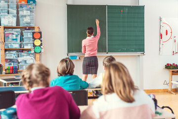 Teacher writing interesting things on blackboard in school while the class is listening © Kzenon