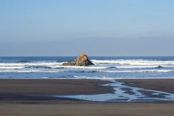 Fototapeta na wymiar Conjunto de rocas en mitad del mar frente a las olas en un día de invierno soleado con el cielo azul. 