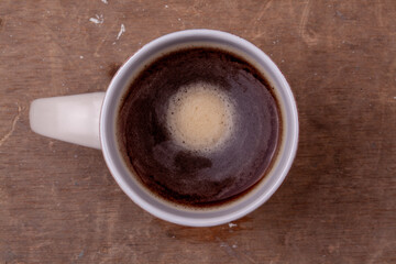 Taza de café solo americano negro en una taza redonda y blanca sobre un fondo marrón de una mesa de madera.