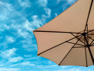Sun patio umbrella against blue sky with some white light clouds, sunny day