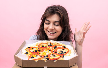 Attractive girl with pizza in a box for delivery on a pink background.