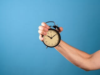 Hurry up, it's time to act, concept. A man's hand holds a vintage alarm clock, a photo on a blue background