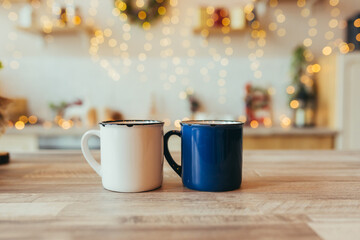 close-up photo of two Christmas cups, on New Year's background, Christmas tree and colorful lights, in the kitchen on the table