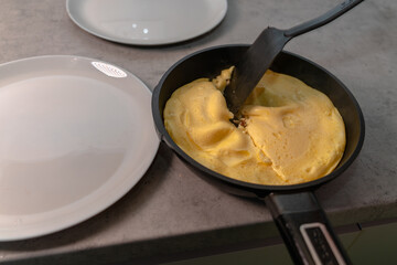 Omelet in a frying pan and two empty plates on the table