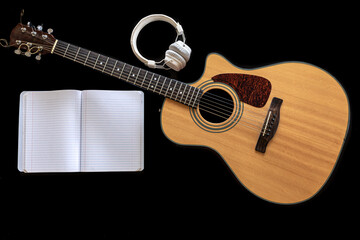 Classical acoustic guitar, headphones and notebook on a black background.