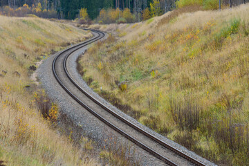 A winding railway track that leads through a mountain valley inside the forest in autumn