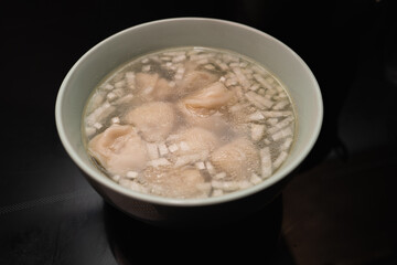 Dumplings with broth and onions in a plate on the black surface of an induction cooker