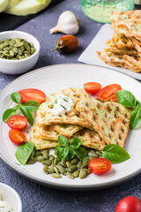 Appetizing zucchini waffles, tomatoes and pumpkin seeds on a plate on the table. Vegetable diet vegetarian food. Vertical view. Close-up