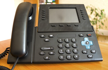 The black desktop push-button telephone. IP phone on desk in office.