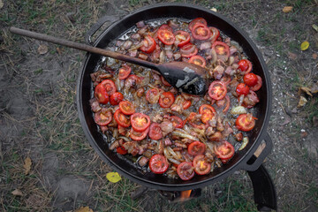 Tomatoes, onions and meat in a pan. Cook at a picnic. A traditional dish. Tomato slices. A fatty dish. Roast vegetables and bacon in a wok. A hearty dinner.