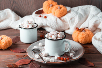 Cocoa and marshmallows in mugs in autumn decorations with pumpkins on a wooden table. Hot sweet drinks