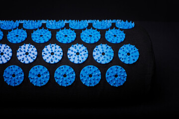 Acupuncture blue mat with many plastic spikes on black background. Alternative therapy and relaxation remedy.