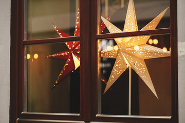 Stylish christmas stars in window, decorations of building or shops in european city street. Modern Christmas festive decor for winter holidays. Sweden illuminated stars. Merry Christmas. Magic time