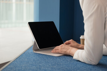 young freelance woman is sitting with a laptop in a public space and working on the Internet. Hands typing on the keyboard of a white thin laptop, close-up