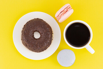 Still life with cup of black coffee and assorted from colorful macaroon cookies and chocolate donut on plate isolated on yellow background. Sweet desserts and espresso cup. Top view