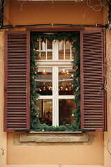 Stylish christmas spruce branches with ornaments and lights decoration on old wooden window of building or shop. Christmas festive decor for winter holidays in european city street. Magic time