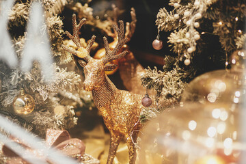 Stylish golden reindeer and modern christmas tree with glitter baubles in window, fairytale...