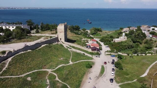 Scenic aerial view of the Tower of ancient ruined Genoese fortress Kaffa against blue sky and dark blue sea. Drone tracking shot, right to left.
