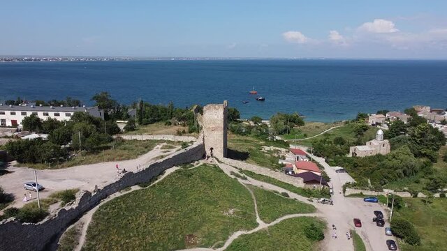 Scenic aerial view of the Tower of ancient ruined Genoese fortress Kaffa against blue sky and dark blue sea. Aerial static drone shot.