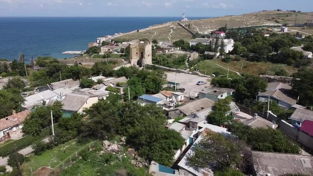 Scenic aerial view of the Tower of ancient ruined Genoese fortress Kaffa against blue sky and dark blue sea. Drone tracking shot, right to left.