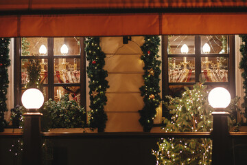 Stylish christmas spruce branches in golden lights illumination on building windows in evening. Atmospheric magic time. Christmas festive decor for winter holidays. Merry Christmas!