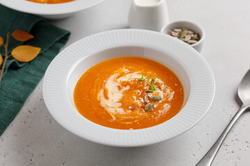 pumpkin soup with seeds and cream in a white plate on a gray table