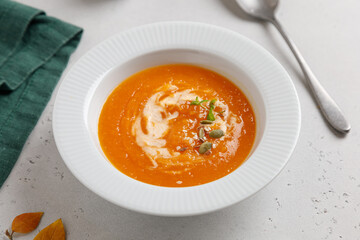 pumpkin soup with seeds and cream in a white plate on a gray table