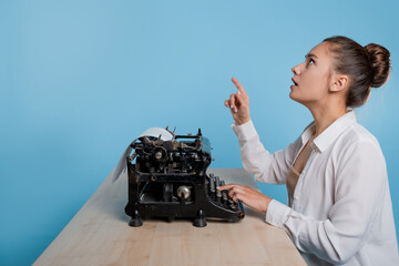 young woman author at a typewriter, writes a text. A writer at a table with a vintage typewriter