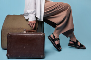 young woman in summer pants and a white shirt is sitting on vintage leather suitcases