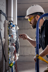 Fototapeta premium A male electrician works in a switchboard with an electrical connecting cable.