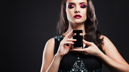 Attractive young brunette woman and a bottle with a new fragrance, use perfume.