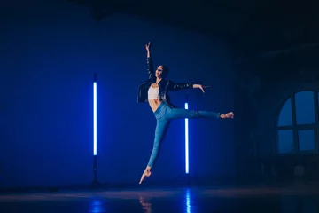 Fotobehang Young woman in casual style - jeans and leather jacket doing ballet in modern studio. Attractive ballerina practices in choreography alone © kohanova1991
