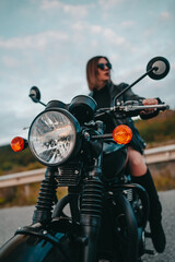 Motorcyclist woman sitting on retro-styled motorcycle. Sexy female driver in jackboots on roadway. Trip, speed, freedom concept.
