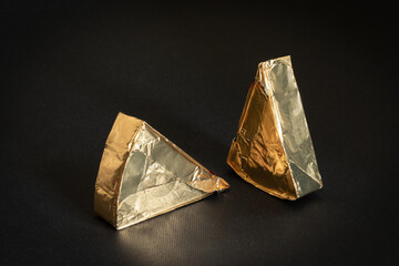 Two triangles of unknown processed cheese in gold foil on a black background