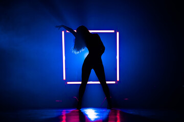 Naklejka na ściany i meble Silhouette of sexy woman dancing on glowing square of led lamps background. She looks seductively. Sexy outfit . Blue smoky studio.